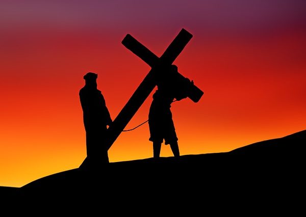 Man carrying a cross up a hill in twilight